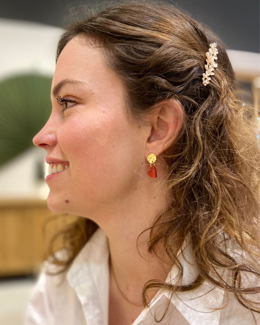 Jeune femme porte ses boucles d’oreilles cœur rouge pailleté. Composées d’un pendentif cœur scintillant et d’un fermoir doré martelé, elles allient élégance et originalité pour sublimer toutes vos tenues.