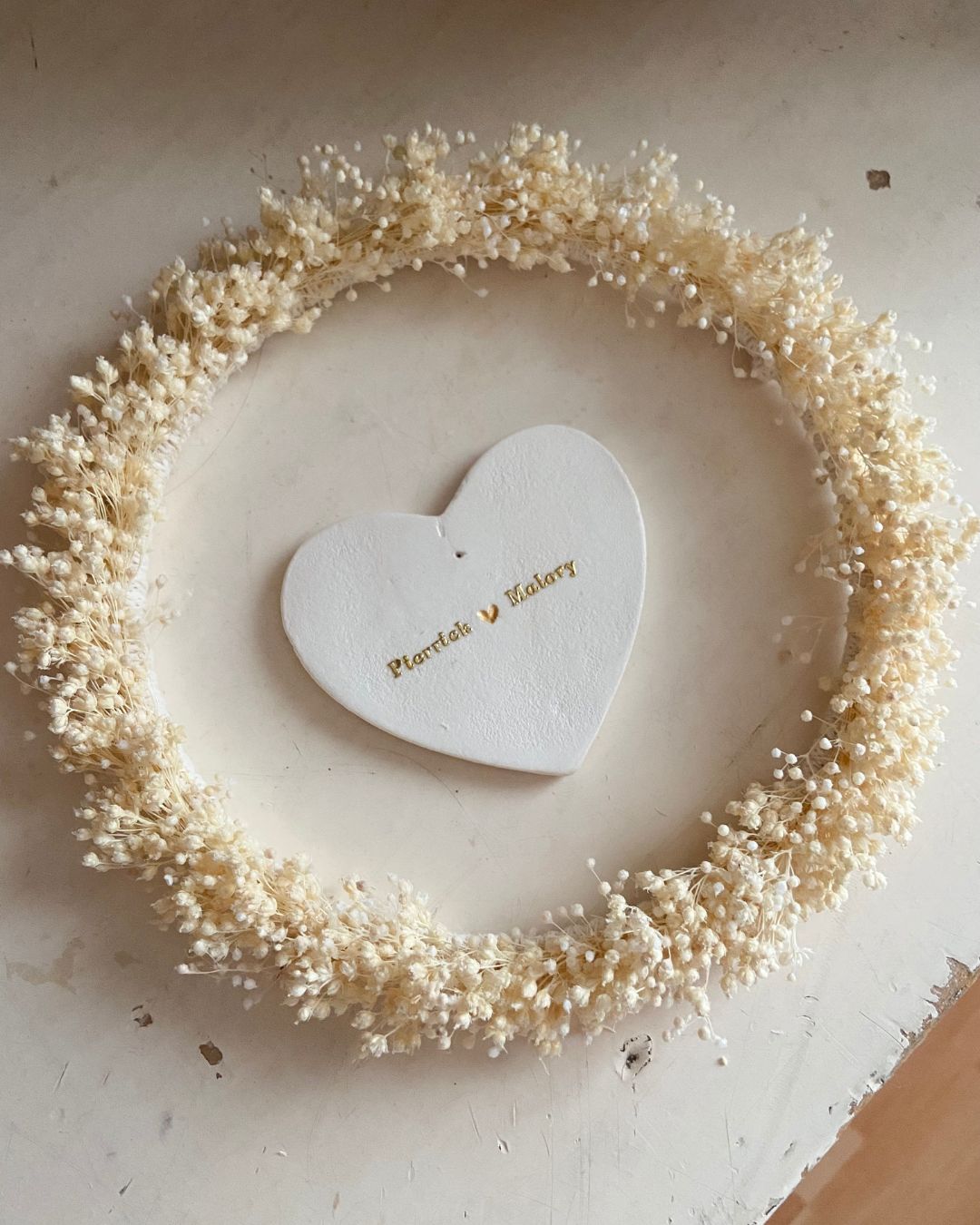 Couronne ronde de 12cm ornée de fleurs séchées blanches fines et d'un coeur en argile personnalisé en son centre fait-main en France par la créatrice Mes attrapes rêves