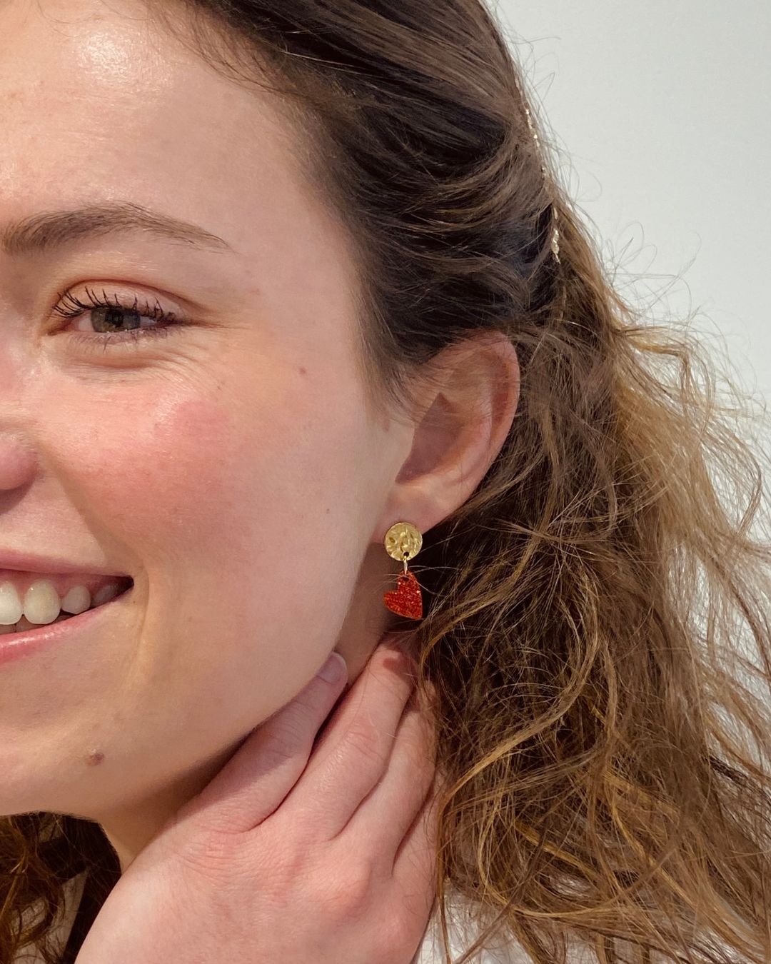 Jeune femme porte ses boucles d’oreilles cœur rouge pailleté. Composées d’un pendentif cœur scintillant et d’un fermoir doré martelé, elles allient élégance et originalité pour sublimer toutes vos tenues.