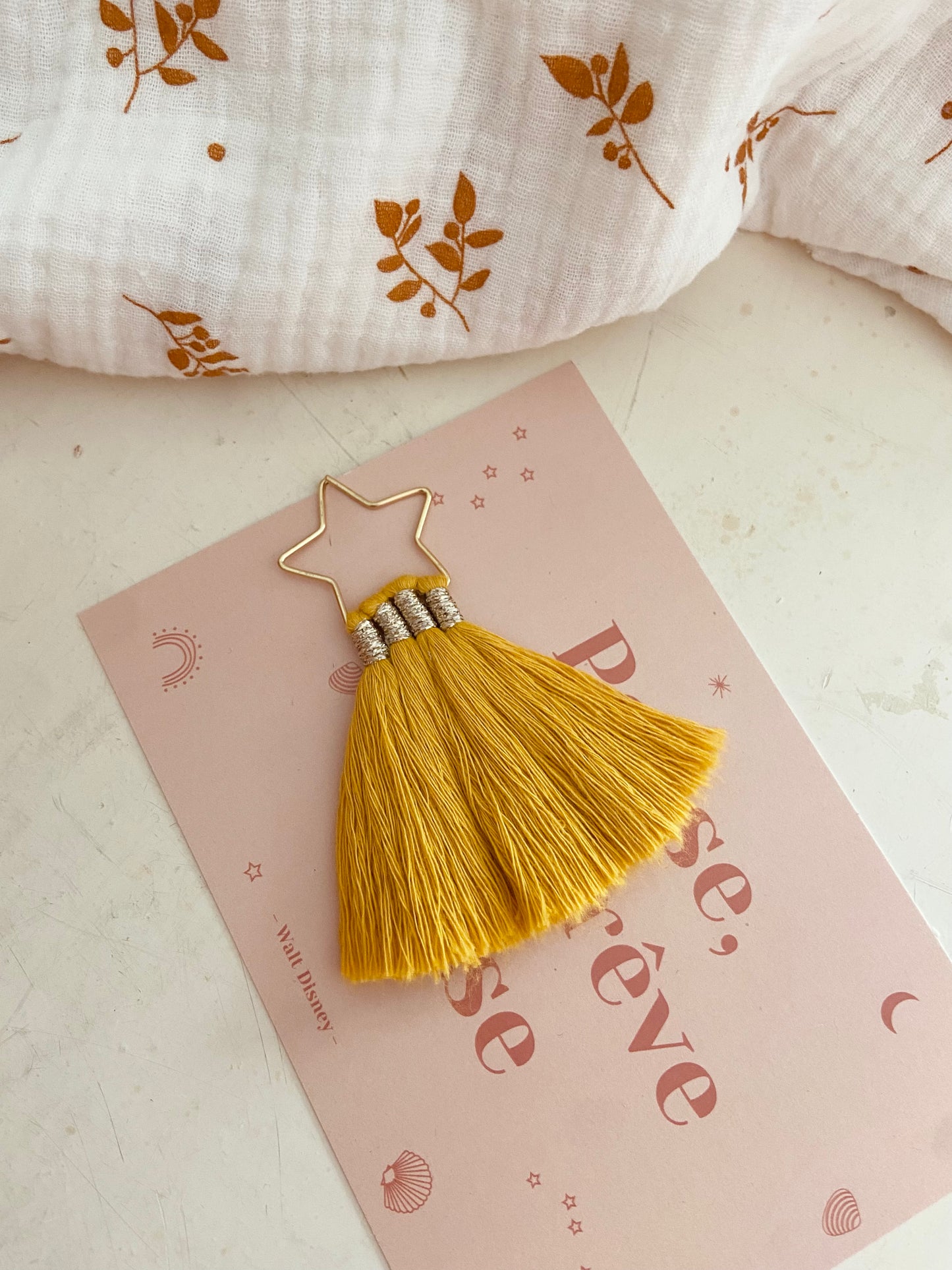 Marque page étoile doré avec pompon coton jaune
Ajoutez une touche de couleur à vos lectures !
Craquez pour notre marque-page en forme d’étoile, orné d'un joli pompon en coton. Fait main avec soin, il est disponible en plusieurs coloris pour s’adapter à tous les goûts. Idéal pour offrir ou se faire plaisir, pour les fans de lecture ou pour les petits cadeaux de fin d'année scolaire, les maîtresses et atsem.