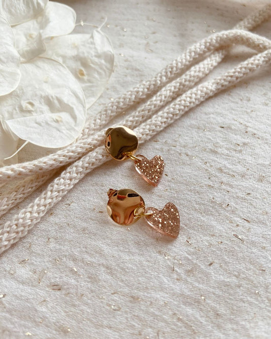 boucles d’oreilles cœur doré pailleté. Composées d’un pendentif cœur scintillant et d’un fermoir doré, elles allient élégance et originalité pour sublimer toutes vos tenues.