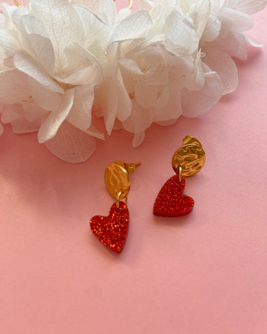 Boucles d’oreilles cœur rouge pailleté. Composées d’un pendentif cœur scintillant et d’un fermoir doré martelé, elles allient élégance et originalité pour sublimer toutes vos tenues.