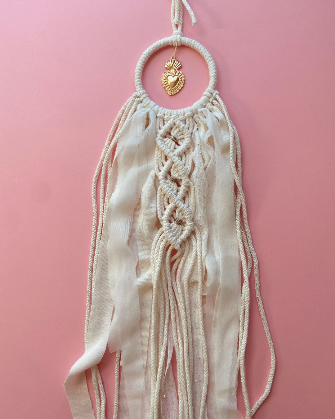 Attrape-rêves en macramé fait main, en corde naturelle et voile beige clair, orné d’un ex-voto cœur doré au centre. Une décoration bohème et élégante, idéale pour une ambiance douce et spirituelle.