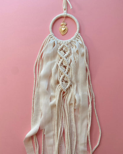 Attrape-rêves en macramé fait main, en corde naturelle et voile beige clair, orné d’un ex-voto cœur doré au centre. Une décoration bohème et élégante, idéale pour une ambiance douce et spirituelle.