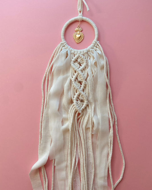 Attrape-rêves en macramé fait main, en corde naturelle et voile beige clair, orné d’un ex-voto cœur doré au centre. Une décoration bohème et élégante, idéale pour une ambiance douce et spirituelle.