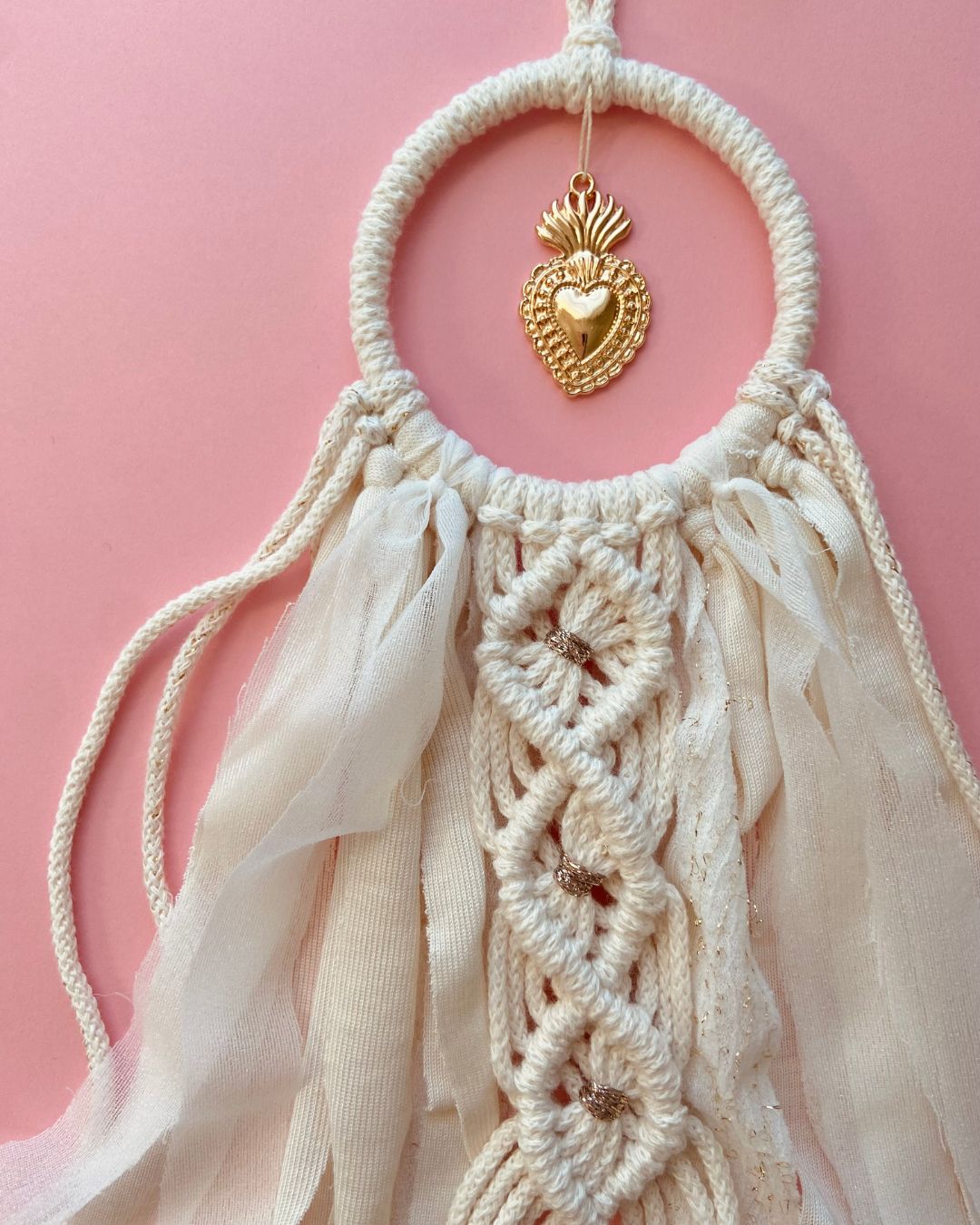 Attrape-rêves en macramé fait main, en corde naturelle et voile beige clair, orné d’un ex-voto cœur doré au centre. Une décoration bohème et élégante, idéale pour une ambiance douce et spirituelle.